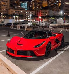 a red sports car parked in a parking lot next to some tall buildings at night