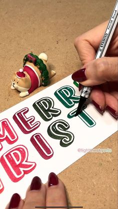 someone is writing merry christmas on a sign with a small toy bear next to it