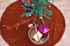 a small christmas tree with presents in a basket on a brown round tablecloth covered floor