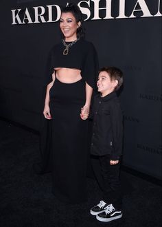 a woman standing next to a little boy in front of a black wall with the words karda shian on it