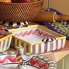 an assortment of colorful ceramic dishes and fruit in a wicker basket on a table