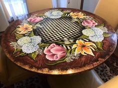 a table with flowers painted on it in the middle of a room next to a window