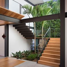 the inside of a modern house with wooden stairs and glass railings, surrounded by greenery