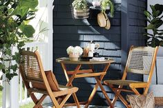 two chairs and a table on a porch with potted plants hanging from the wall