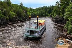 a large boat traveling down a river next to a lush green forest filled with trees