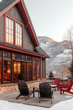 two red chairs sitting in front of a house with snow on the ground and mountains in the background