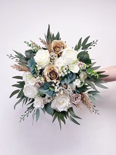 a bridal bouquet with white flowers and greenery is held by someone's hand