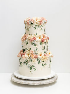 a three tiered wedding cake with flowers on the top and bottom, sitting on a platter