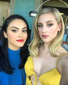 two women posing for the camera with one wearing a blue shirt and yellow dress, while the other wears red lipstick