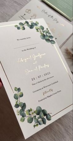 a person holding up a wedding card with greenery on the front and back side