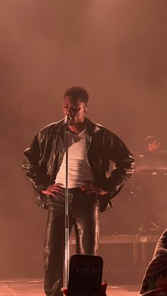 a man standing in front of a microphone on stage with his hands behind his back