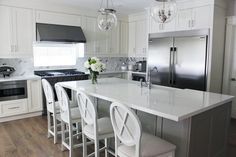 a kitchen with white cabinets and an island in the middle, surrounded by four bar stools