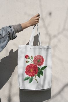 a person holding a tote bag with red flowers on the front and green leaves on the back