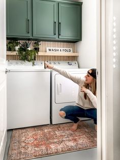 a woman squatting on the floor in front of a washer and dryer