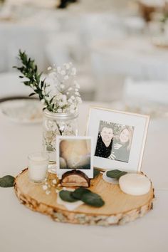 a table topped with pictures and candles on top of a wooden slice covered in greenery