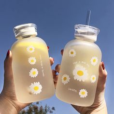 two people holding up jars with flowers painted on the lids and one has a straw in it