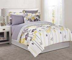 a white bed with yellow and gray flowers on the comforter is in front of a window