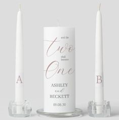 two white candles sitting next to each other on top of a glass stand with the words,