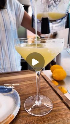 a person pouring a drink into a glass on top of a wooden table next to lemons