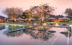 an outdoor swimming pool with chaise lounges and trees in the background at dusk