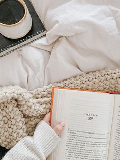 someone is reading a book in bed next to a cup of coffee and an alarm clock