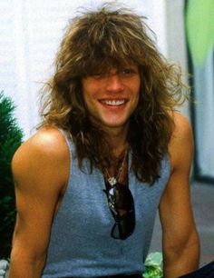 a man with long hair sitting next to a christmas tree and smiling at the camera