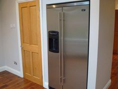 a stainless steel refrigerator in the corner of a room with hardwood floors and white walls