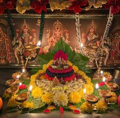 an arrangement of flowers and candles in front of a wall with paintings on it,