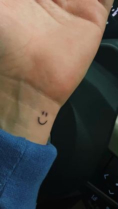 a smiley face tattoo on the wrist is shown in black ink, and has a small smile