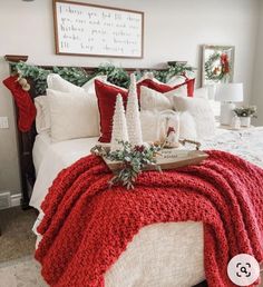 a bed covered in red and white blankets with christmas decorations on the headboard,