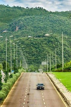 a car is driving down the road in front of some hills and telephone poles on either side