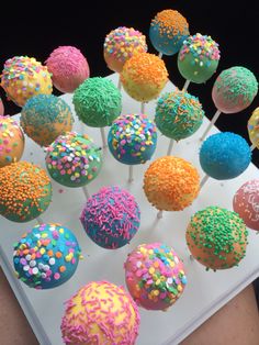 cake pops with sprinkles are arranged on a white tray in front of a black background