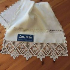 an embroidered tablecloth with white lace on it sitting on a wooden floor in front of a wood floor