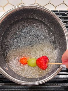 two strawberries and one green apple are in a silver bowl on top of the stove