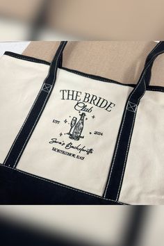 a white and black tote bag with the bride embroidered on it's side