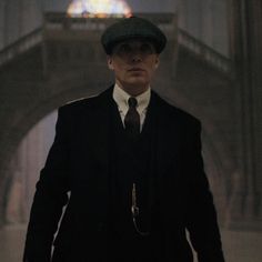 a man in a suit and tie standing under a bridge with a stained glass window behind him