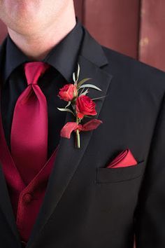 a man wearing a black suit with red flowers on it's lapel flower