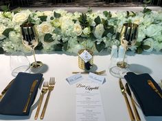 the table is set with place settings and gold utensils, along with white flowers