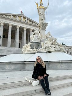 a woman sitting on steps in front of a building with a large statue behind her