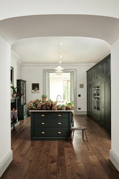 a kitchen with wooden floors and green cabinets in the center, along with an arched doorway leading to another room