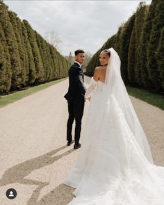 a bride and groom standing in the middle of a road with hedges on either side