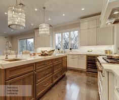 a large kitchen with wooden floors and white cabinets is pictured in this image, there are chandeliers hanging from the ceiling