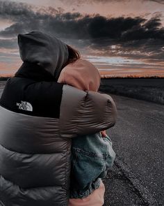 a person wearing a hooded jacket is sitting on the side of an empty road at dusk