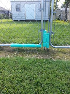 a blue pipe is in the grass behind a chain link fence with a house in the background