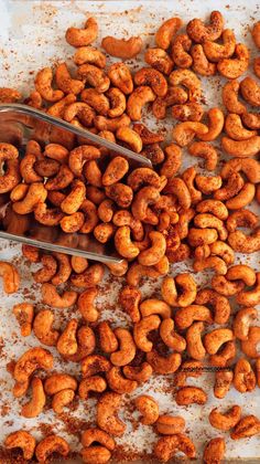 a tray full of roasted cashews with a spoon resting on the ground next to them