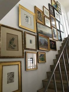 there are many framed pictures on the wall next to the stair case in this house