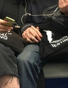 a woman sitting on a bench looking at her cell phone while wearing headphones and holding a t - shirt