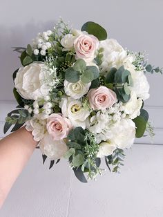 a bouquet of white and pink flowers is being held by someone's hand in front of a wall