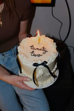 a woman holding a birthday cake with a lit candle on it that reads twenty two