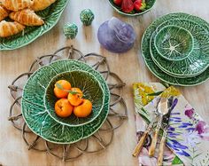 a table topped with green plates and bowls filled with fruit next to croissants